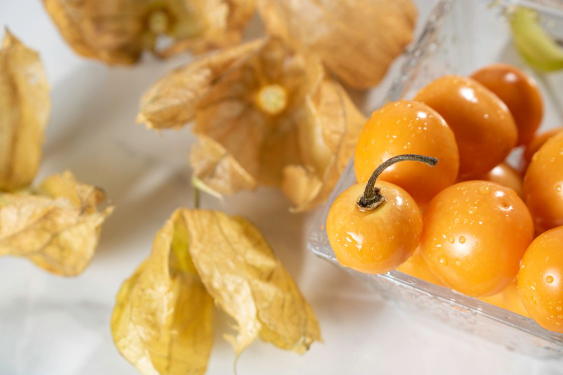 Orange Cape gooseberries in a glass container with papery husks around them